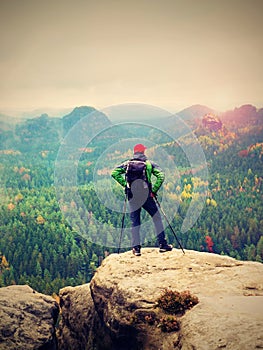 Tourist guide on the summit with poles in hand and heavy backpack. Hiker green jakcet nad red cap