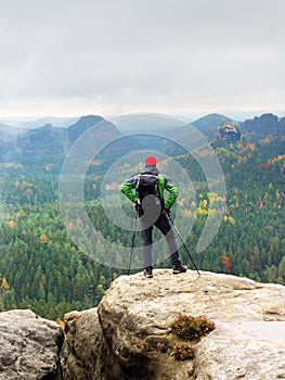 Tourist guide on the summit with poles in hand and heavy backpack. Hiker green jakcet nad red cap