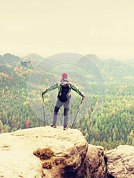 Tourist guide on the summit with poles in hand and heavy backpack. Hiker green jakcet nad red cap