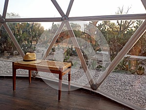 Tourist hat on a handmade woven bench with large window of the geodesic tent for glamping