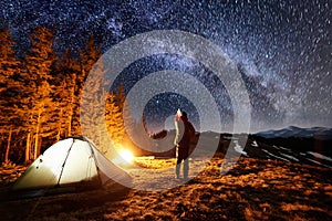 Tourist have a rest in his camp near the forest at night, pointing at beautiful night sky full of stars and milky way