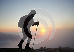 Tourist hiker man with backpack on rocky mountain on misty blue sky and raising sun background.
