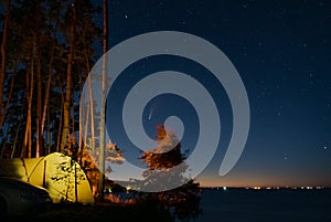 Tourist hikers tent near the lake at night with stars and Neowise comet with light tail in dark night sky