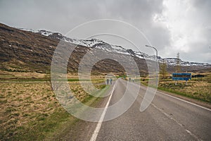 Tourist hiking next to the street and walking in the direction of Seydisfjordur, snow mountain range in the background, Iceland