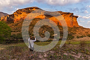 Tourist holding smart phone and taking photo at scenic cliff illuminated by sunset light in the majestic Golden Gate Highlands Nat