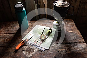 Tourist items in the hut. Knife, map and compass on the table. Light from the window onto the table. Items on the table