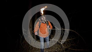A tourist lost in the woods. A man in a bright jacket and with a burning torch in his hands goes at night through a