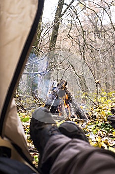Tourist lying in tent and looking at the fire in the mountain forest