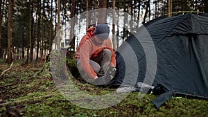 Tourist makes camp in woods, sets up tent in meadow in fall forest, prepares for an overnight stay in campsite