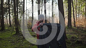 Tourist makes camp in woods, sets up tent in meadow in fall forest, prepares for an overnight stay in campsite