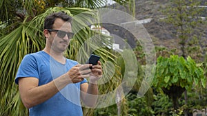 Tourist man checking his email with serious face in a tropical using internet and thinking. Boy holding cellphone in vacation with