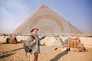 Tourist man in hat with camel background pyramid of Egyptian Giza, sunset Cairo, Egypt