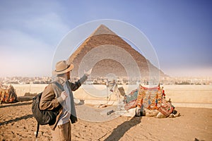 Tourist man in hat with camel background pyramid of Egyptian Giza, sunset Cairo, Egypt