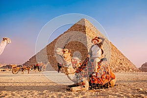 Tourist man with hat riding on camel background pyramid of Egyptian Giza, sunset Cairo, Egypt