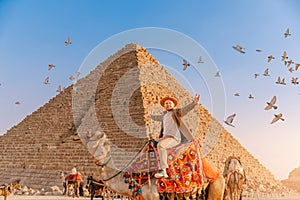 Tourist man with hat riding on camel background pyramid of Egyptian Giza, sunset Cairo, Egypt