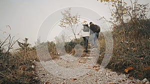 Tourist man on a hiking adventure taking wife's hand helping her climb up a mountain