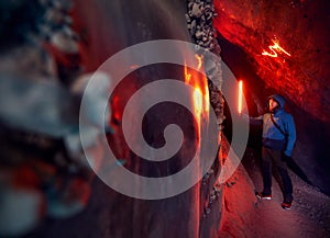 Tourist man holding red glow lamp in deep narrow glacial ice cave