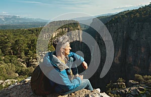 Tourist man sitting on cliff and overlooking big canyon, panoramic view