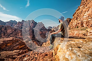 Tourist man sitting on the rock at the red rocky mountains in Petra. Jordan