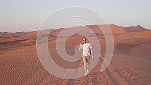 Tourist man in sunglasses walking in sand dunes in red desert in UAE.