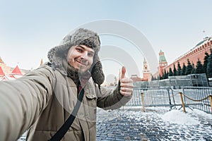 Tourist man takes a photo of himself against the background of a red square in winter in Moscow, Russia