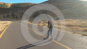 Tourist man walking on center of mountain road on sunset. Joyful guy having adventure in mountains.