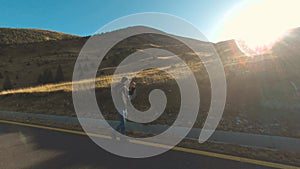 Tourist man walking on center of mountain road on sunset. Joyful guy having adventure in mountains.