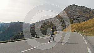 Tourist man walking on center of mountain road on sunset. Joyful guy having adventure in mountains.