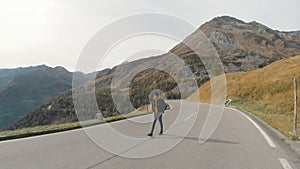 Tourist man walking on center of mountain road on sunset. Joyful guy having adventure in mountains.