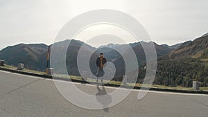 Tourist man walking on center of mountain road on sunset. Joyful guy having adventure in mountains.