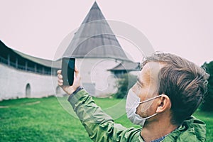 Tourist man wearing medical mask taking photo on smartphone while on tour in historical castle. New normal, tourism during
