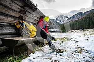 A tourist man in a yellow cap and a red down jacket puts crampons on his boots.