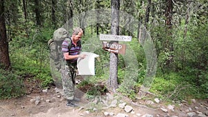 Tourist with a map near the signs. Inscriptions Tungur village, Kara Turek mountain.