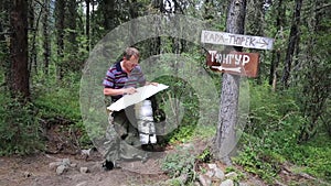 Tourist with a map near the signs. Inscriptions Tungur village, Kara Turek mountain.