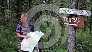 Tourist with a map near the signs. Inscriptions Tungur village, Kara Turek mountain.