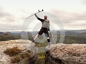 Tourist with medicine crutch above head achieved mountain peak. Hiker with broken leg