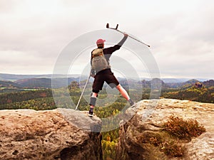 Tourist with medicine crutch above head achieved mountain peak. Hiker with broken leg