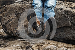 Tourist in old worn out hiking boots and blue jeans in a rough mountain terrain. Long journey concept. Legs in old shoes on hard