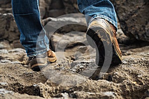 Tourist in old worn out hiking boots and blue jeans in a rough mountain terrain. Long journey concept. Legs in old shoes on hard