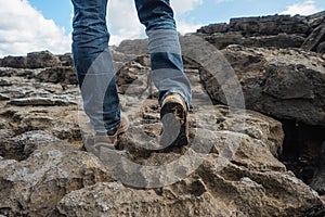 Tourist in old worn out hiking boots and blue jeans in a rough mountain terrain. Long journey concept. Legs in old shoes on hard