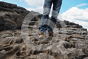 Tourist in old worn out hiking boots and blue jeans in a rough mountain terrain. Long journey concept. Legs in old shoes on hard