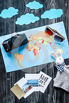 Tourist outfit and camera with map for trip with kids dark wooden background top view mockup