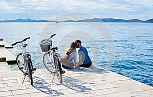Tourist pair, man and woman with bicycles on high paved stone sidewalk near sea water on sunny day
