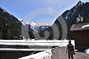 A tourist passing by a small water dam with wooden house near by tourist path heading directly towards to Murg lakes