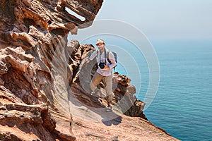 Tourist photographer climbs the cliff above sea, Hormuz Island,
