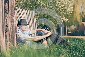 Tourist photographer is resting sitting on the grass near the old fence. Post processing photo