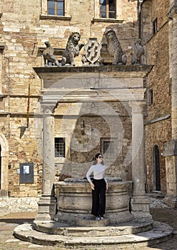 Tourist posing at The well of Griffins and Lions in the big square of Montepulciano, Italy.