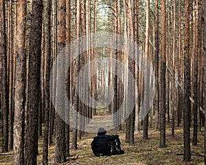 Tourist resting in the forest. Traveler man hugs a backpack and looks in the Sun. Camping scene in the wild. Toned. Copy space