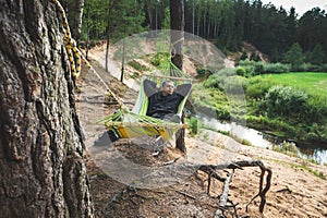 A tourist is resting in a hammock in a picturesque place on the steep bank of the river