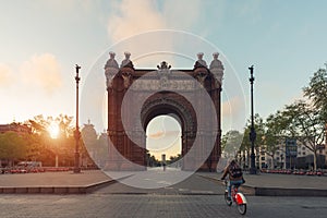 Tourist riding bicycle near Bacelona Arc de Triomf during sunrise in the city of Barcelona in Catalonia, Spain.